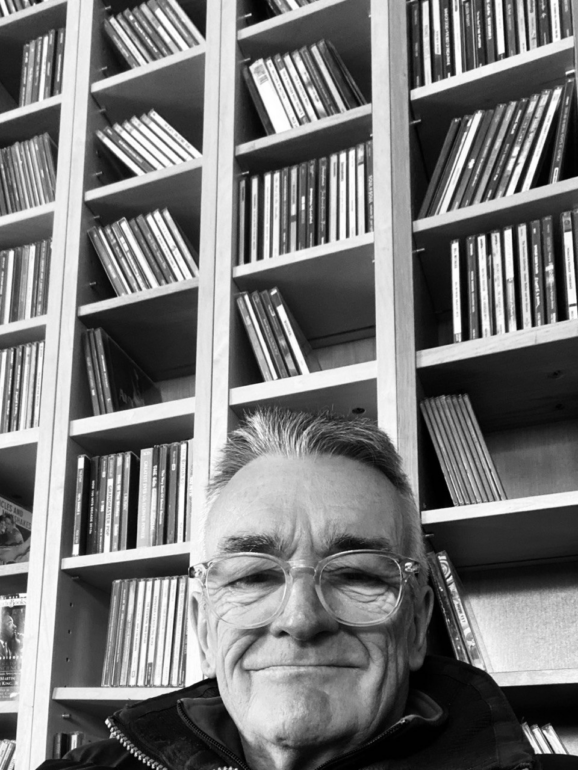 Black and white photo of Robbie Cassels in front of a rack of CDs.